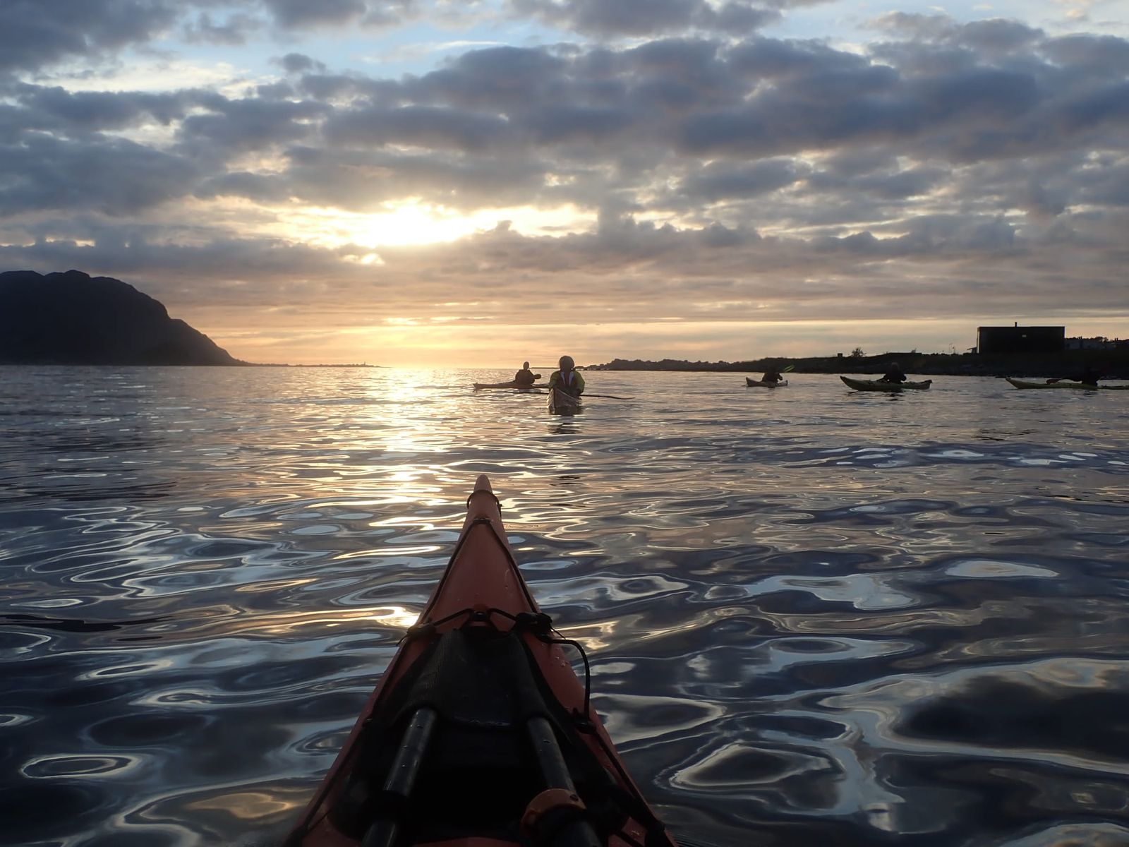 Solnedgang bak fjellene med padlegruppe på vannet på Ellingsøyfjorden